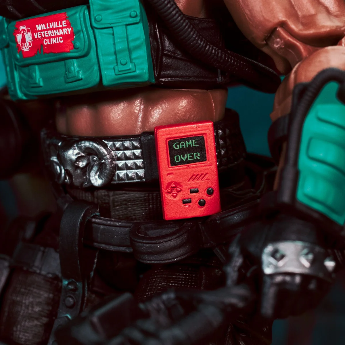 A close-up of Flatline's belt, showing a green pouch marked Millville Veterinary Clinic and a red handheld games console reading GAME OVER